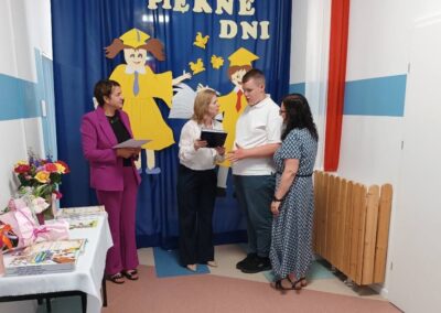 Grupa nauczycielek trzyma bukiety kwiatów przed dekoracją uroczystości.