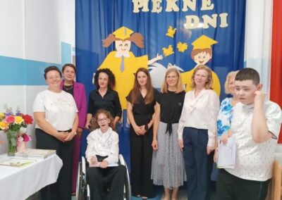 Uczniowie i nauczyciele ustawieni razem przed szkolną dekoracją.