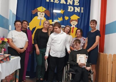 Nauczyciele i uczniowie pozują razem na tle dekoracji.