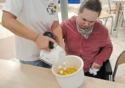 Instruktorka używa miksera ręcznego do przygotowania masy, a uczestniczka obserwuje proces