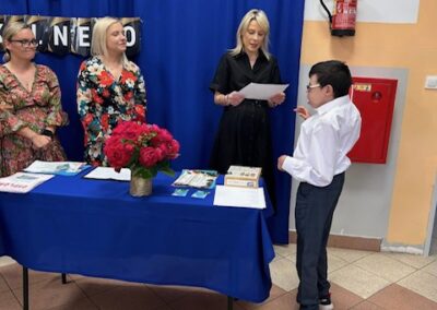 Uczeń trzyma dyplom, a obok stoją nauczyciele podczas zakończenia roku szkolnego.