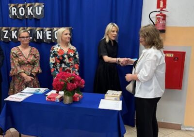 Uczeń odbiera wyróżnienie, a w tle widać dekorację zakończenia roku szkolnego.