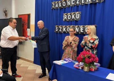 Nauczyciele wręczają uczniowi dyplom podczas oficjalnej części zakończenia roku.