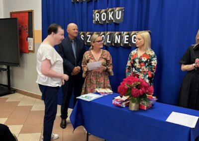 Uczeń odbiera dyplom i gratulacje od nauczyciela podczas szkolnej uroczystości.