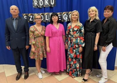 Zdjęcie grupowe nauczycieli i uczestników uroczystości na szkolnej sali podczas zakończenia roku.